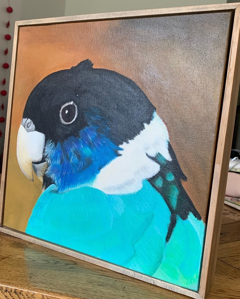 Framed painting of a colorful ringneck parrot on a wooden surface
