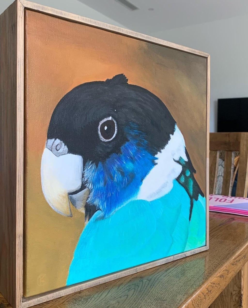 Framed painting of a Ringneck  parrot on a wooden table