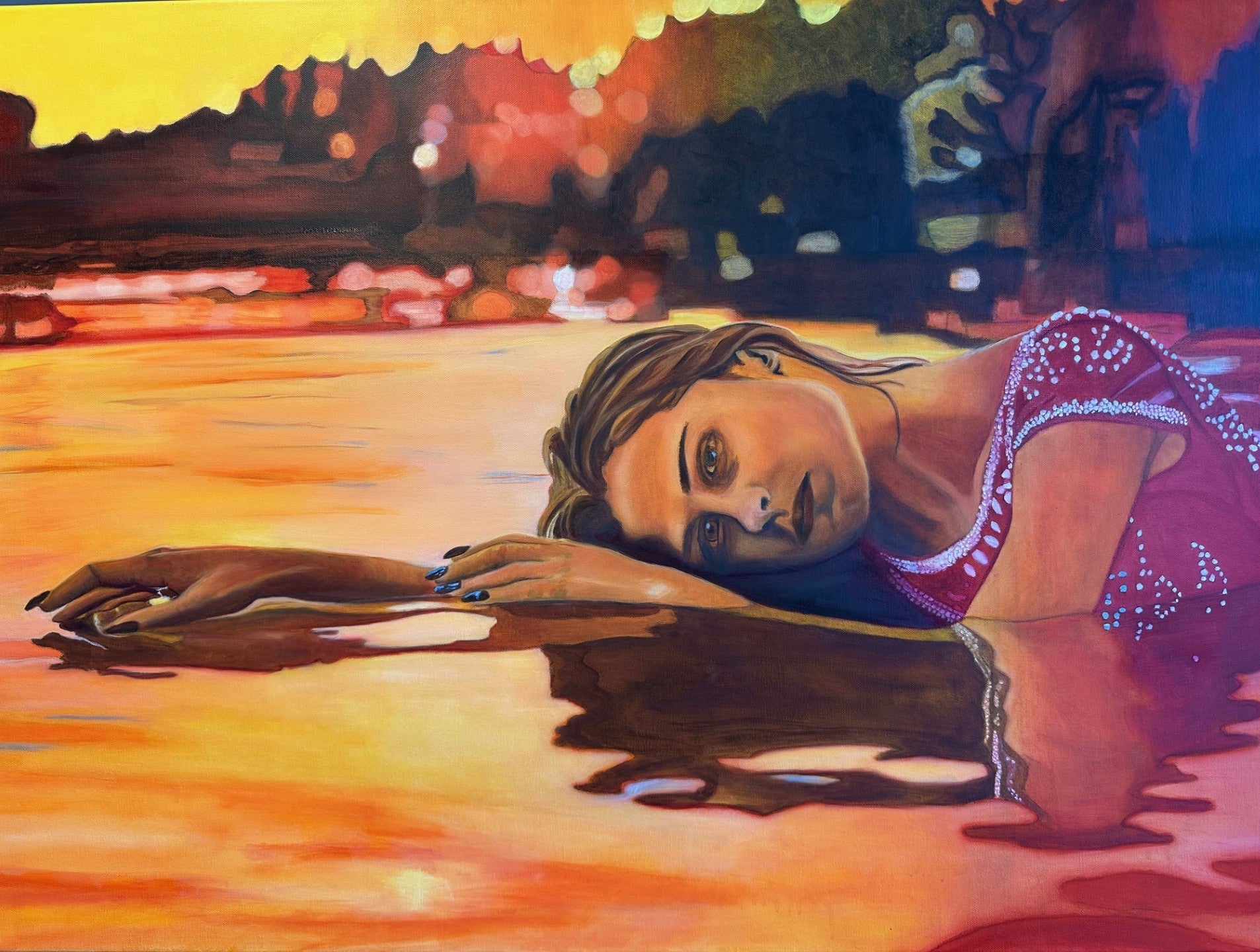 Woman lying in the water near the beach with a colorful sunset in the background